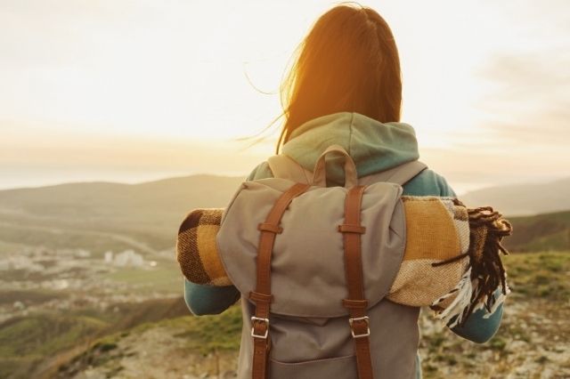 mujer mirando el amanecer con un bolso de viaje