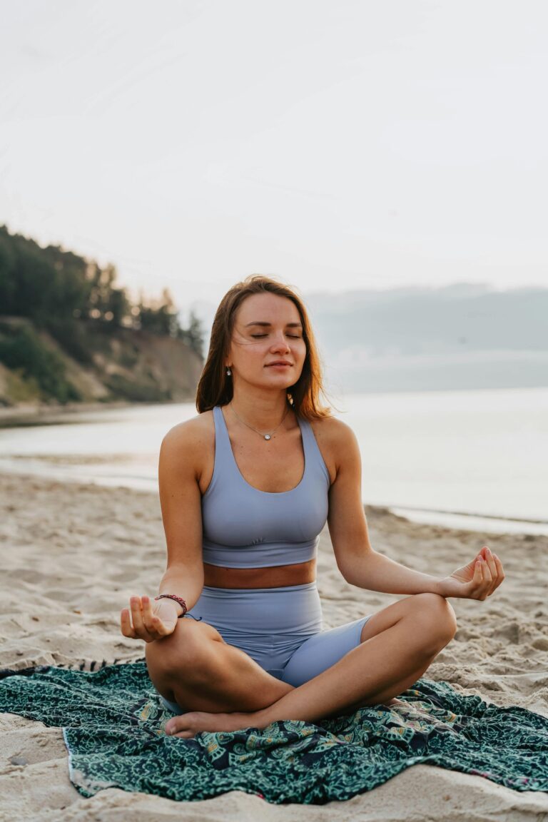 Mujer sentada en la arena de playa en posición de loto meditando